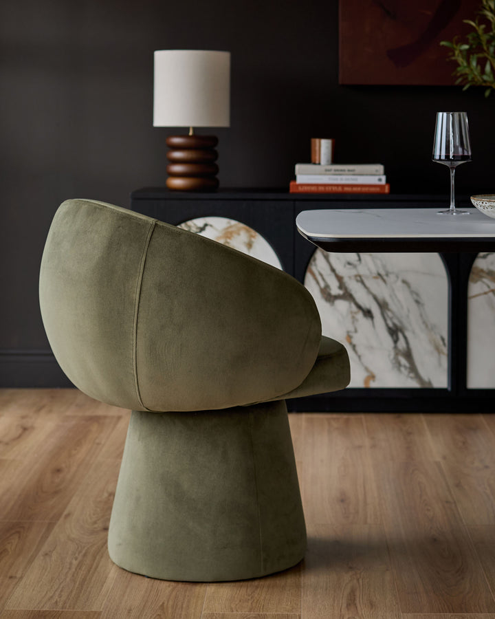 Darcy swivel dining chair in olive green velvet, shown from a side angle in a modern dining room setting.