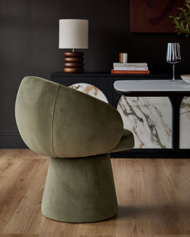 Darcy swivel dining chair in olive green velvet, shown from a side angle in a modern dining room setting.