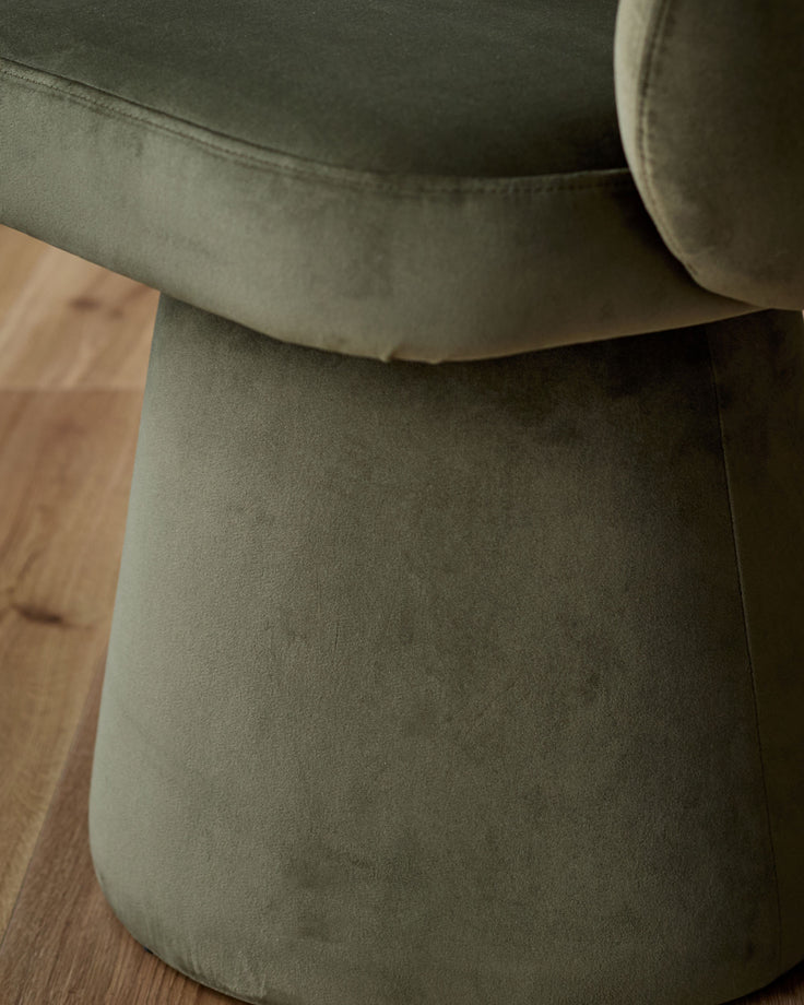 Darcy swivel dining chair in olive green velvet, viewed from above showing curved seat and wooden floor detail.