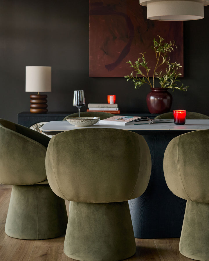 Darcy swivel dining chair in olive green velvet, shown at dining table with rounded backrest and cylindrical base.