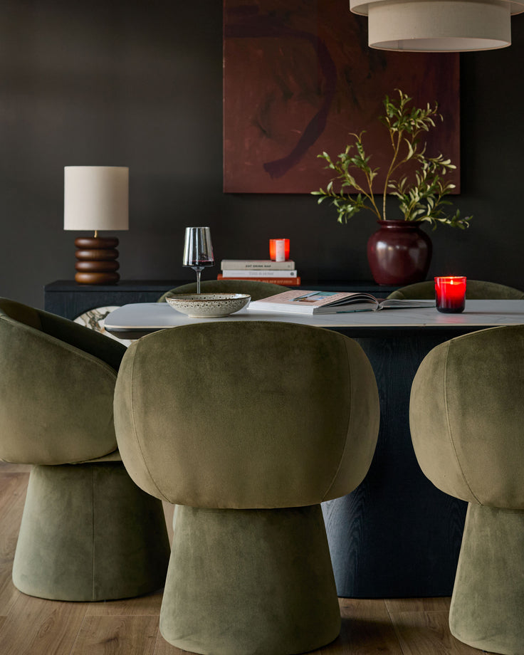 Darcy swivel dining chair in olive green velvet, shown at dining table with rounded backrest and cylindrical base.