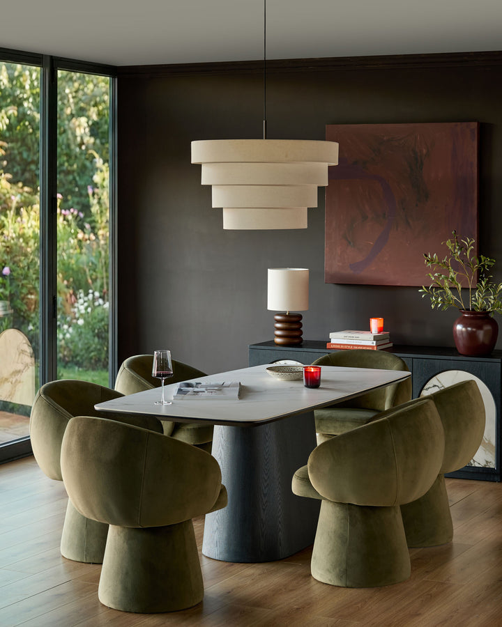 Darcy swivel dining chair in olive green velvet, shown in a modern dining room setting around a white table.