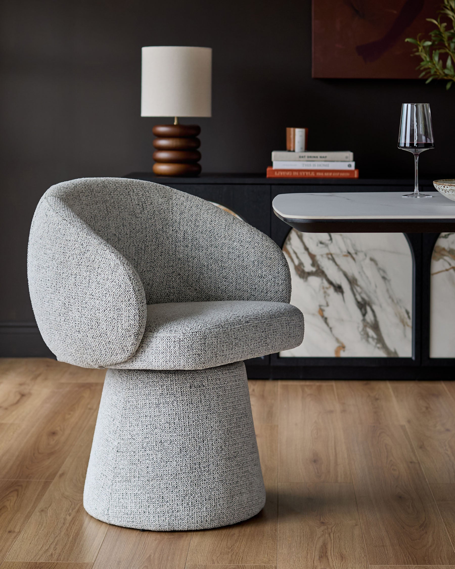 Darcy grey fabric swivel dining chair with curved back and pedestal base, shown in a styled room setting.