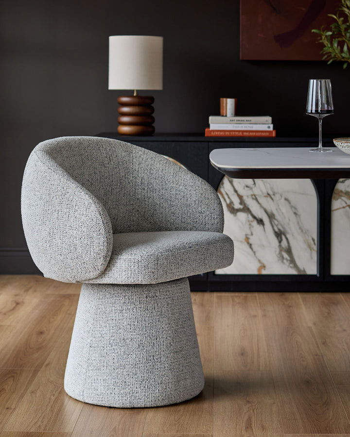 Darcy grey fabric swivel dining chair with curved back and pedestal base, shown in a styled room setting.