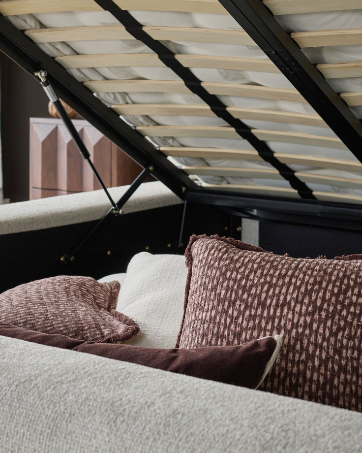 Darla king-size ottoman bed in natural fabric with brown textured pillows, viewed from side angle with open storage mechanism.