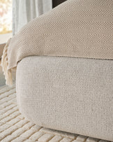 Darla King-Size Ottoman Bed in Natural fabric, showing textured upholstery detail and herringbone throw blanket from side angle.