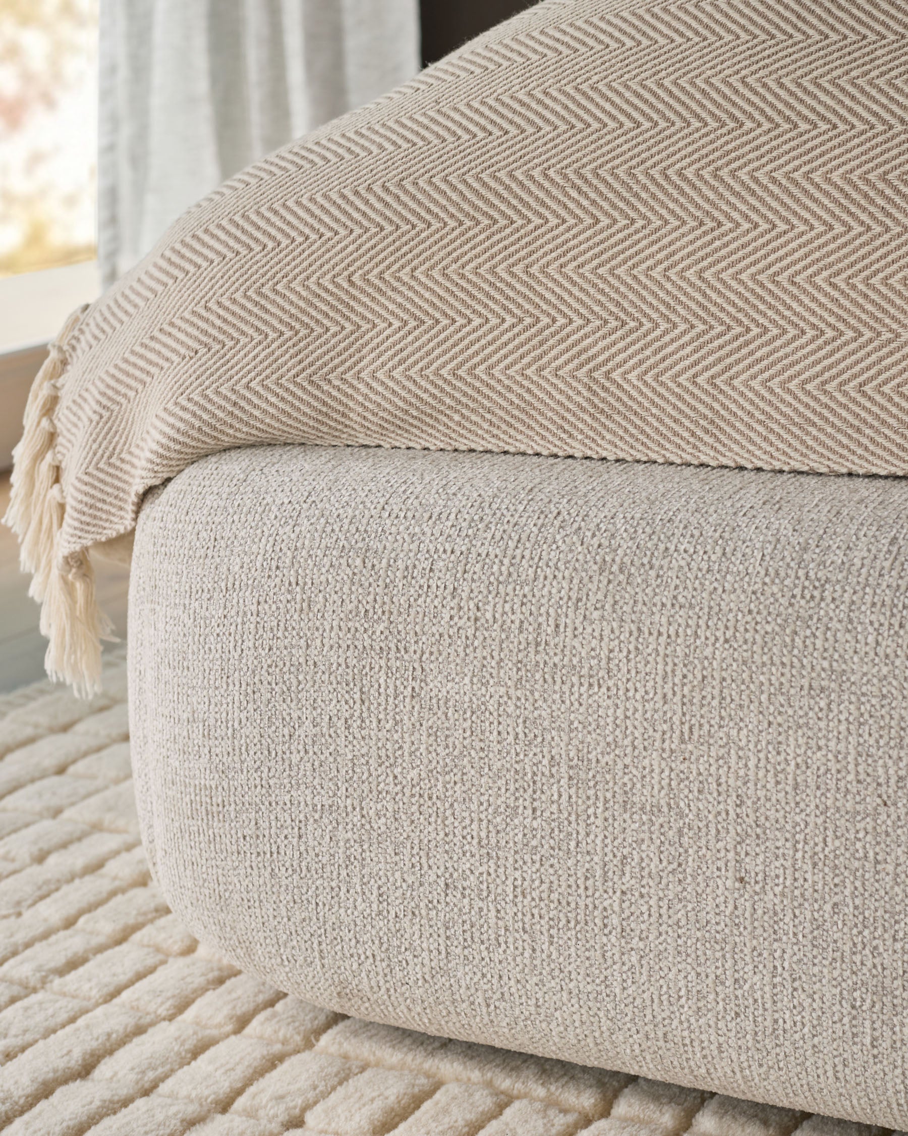 Darla King-Size Ottoman Bed in Natural fabric, showing textured upholstery detail and herringbone throw blanket from side angle.