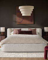 Darla King-Size Ottoman Bed in natural fabric, shown in a styled bedroom with burgundy accents and pendant lighting.