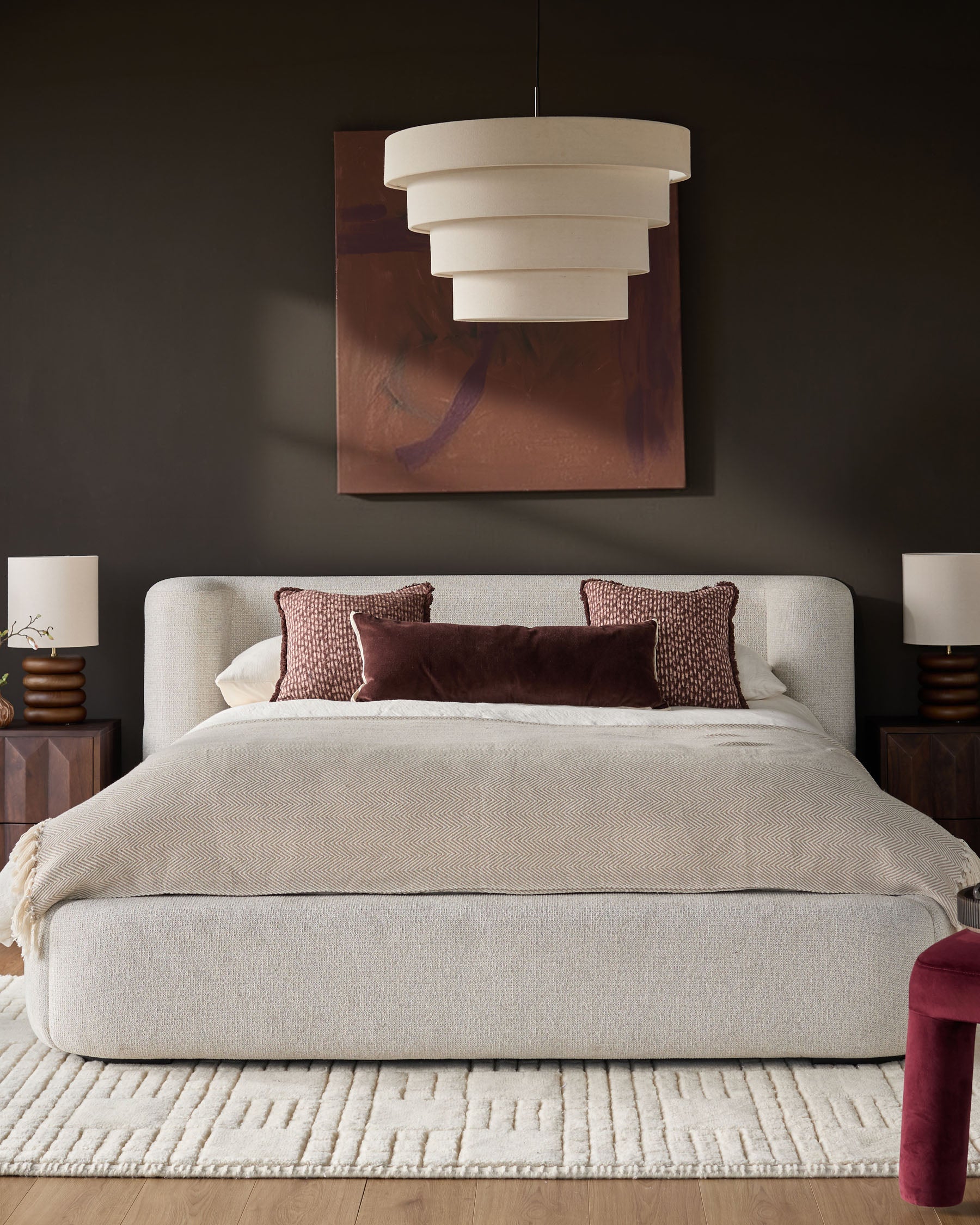 Darla King-Size Ottoman Bed in natural fabric, shown in a styled bedroom with burgundy accents and pendant lighting.