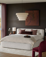 Darla king-size ottoman bed in natural fabric, shown in a styled bedroom with burgundy accents and pendant lighting.