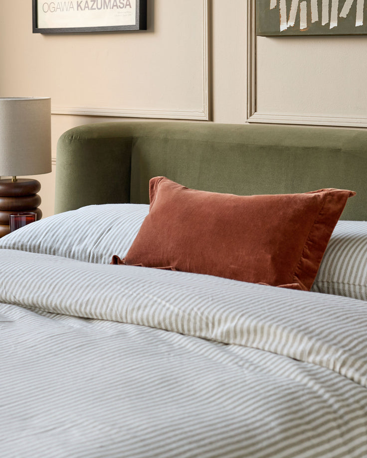 Olive green velvet ottoman bed with striped bedding and rust-colored pillow in modern bedroom setting.