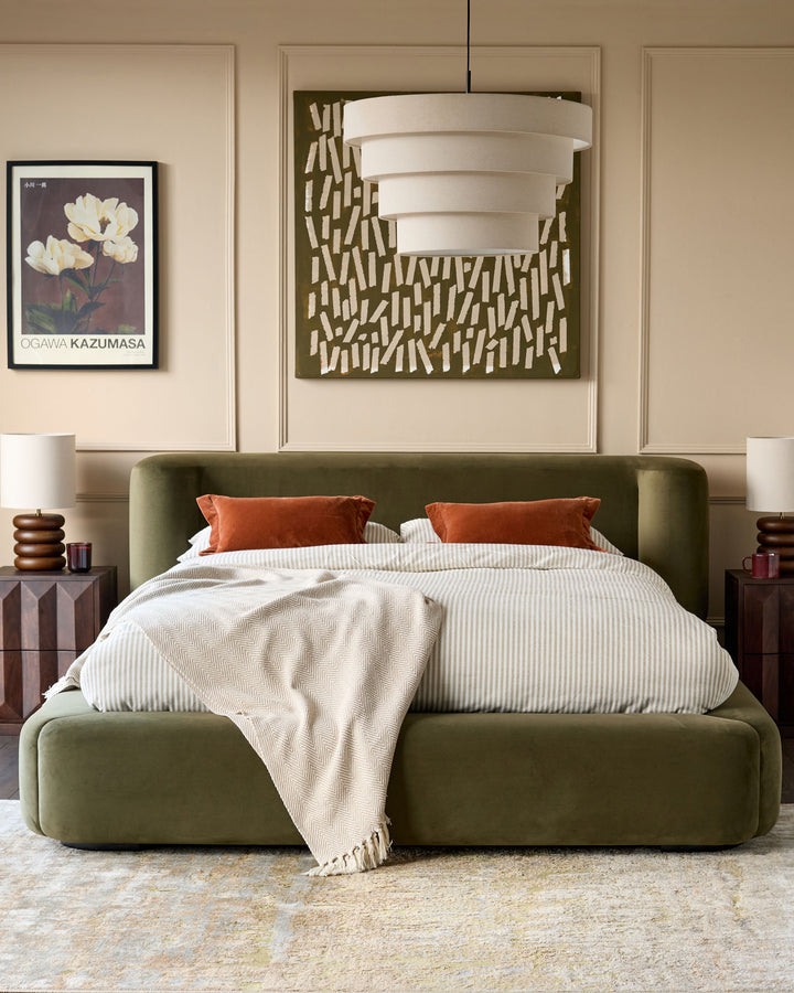 Darla King-Size Ottoman Bed in olive green velvet, shown with striped bedding and rust pillows in a styled bedroom setting.