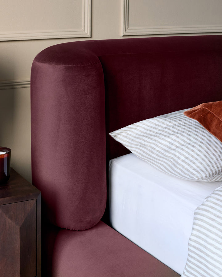 Darla King-Size Ottoman Bed in plum velvet, showing rounded headboard and bedding detail from side angle.