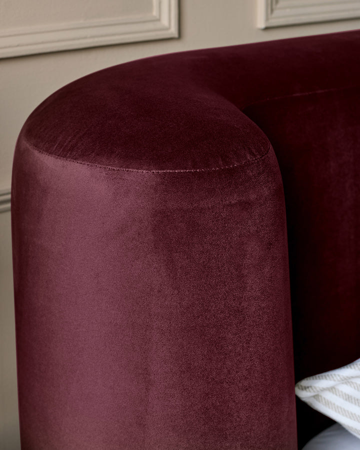 Darla King-Size Ottoman Bed in plum velvet, showing rounded cylindrical footboard with stitched seam detail and soft upholstered finish.