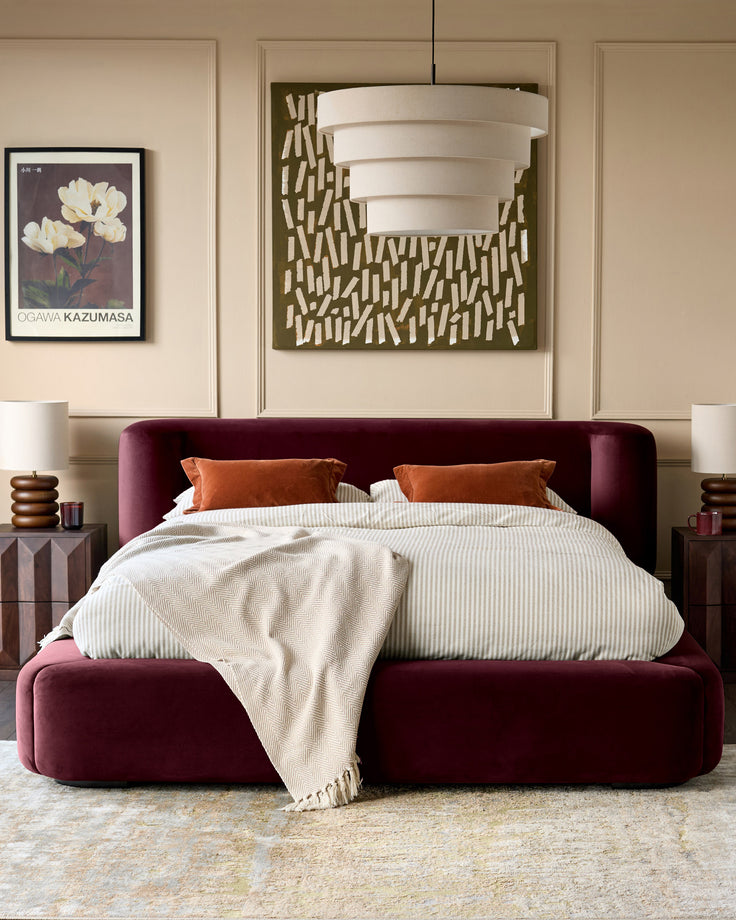 Darla king-size ottoman bed in plum velvet, styled in a bedroom with neutral bedding and orange accent pillows.