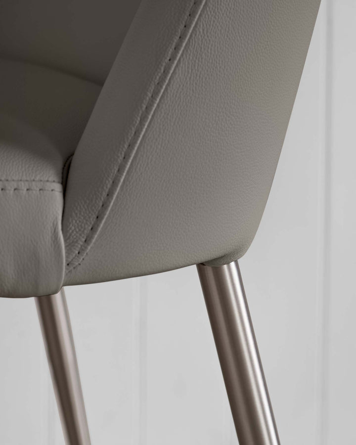 Close-up of a grey, faux-leather chair with a brushed metal leg. Features stitched detailing.