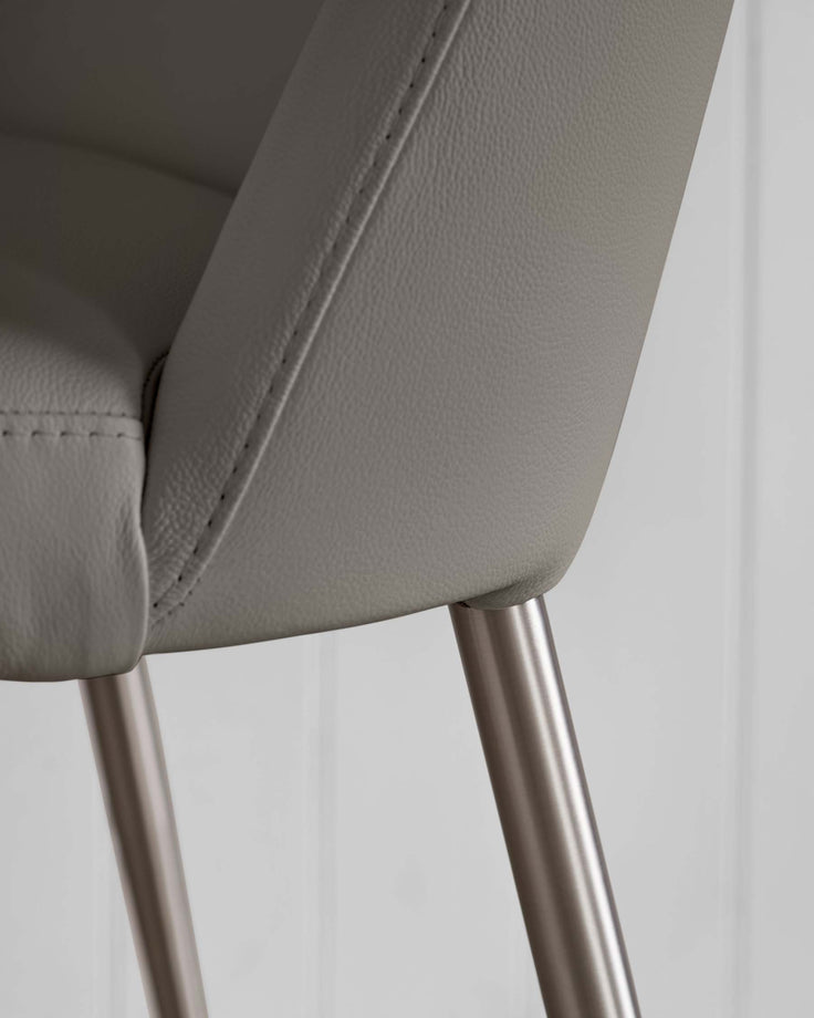 Close-up of a grey, faux-leather chair with a brushed metal leg. Features stitched detailing.
