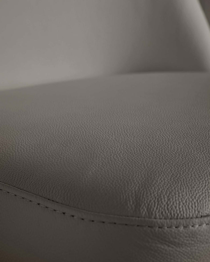 Close-up of a grey upholstered chair with visible stitching along the edge, showcasing the texture and detail of the material.