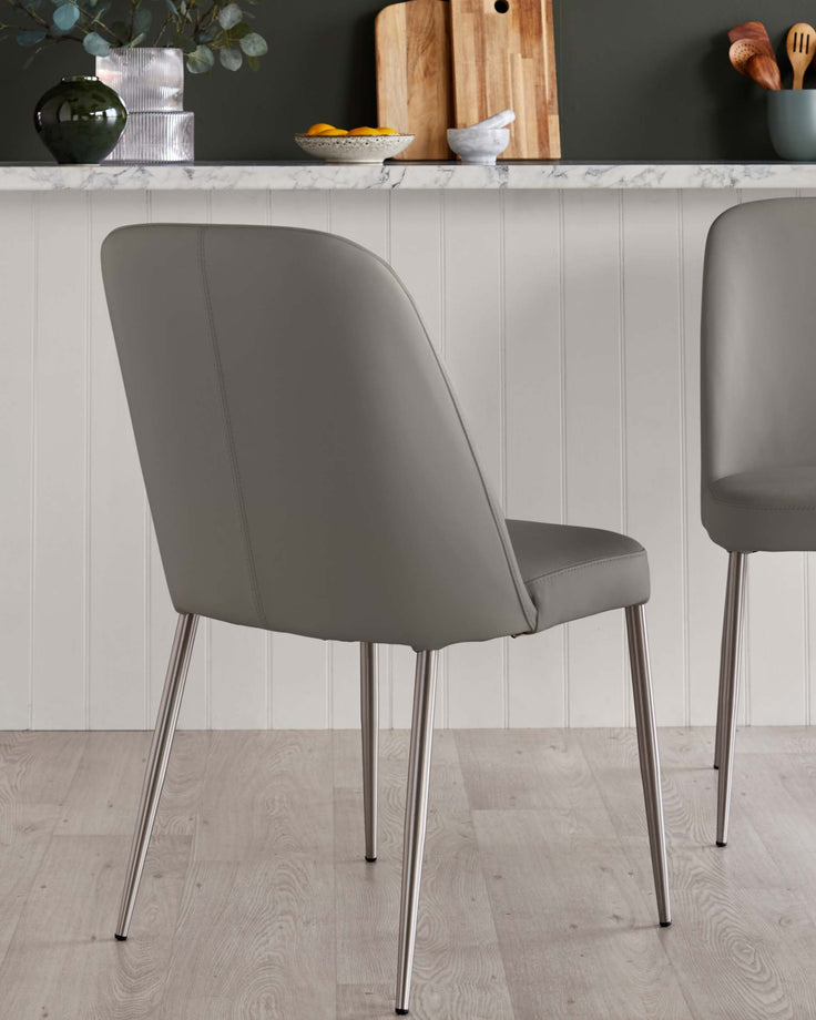 Two grey dining chairs with metal legs sit in front of a kitchen counter, providing a modern and sleek aesthetic.