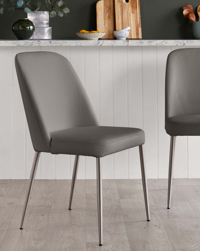 A pair of grey dining chairs with metal legs sit on a wooden floor, in front of a counter top with decor.