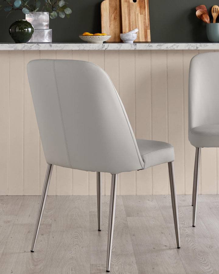 Two modern dining chairs with light grey faux leather upholstery and brushed metal legs, photographed in a kitchen setting.