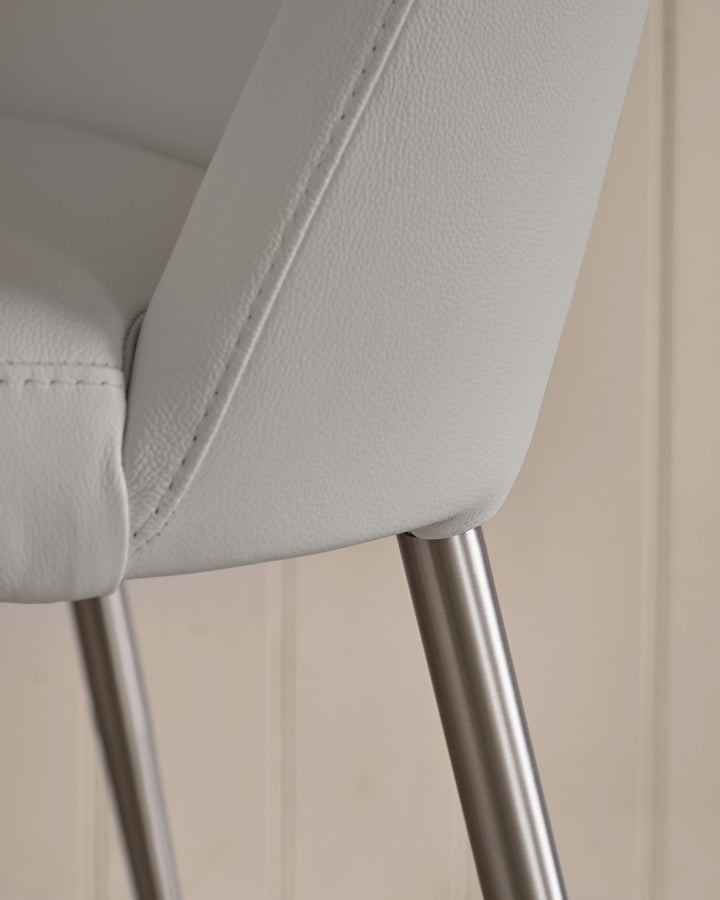 Close-up of a modern, light grey leather chair with sleek, brushed metal legs against a neutral wall.