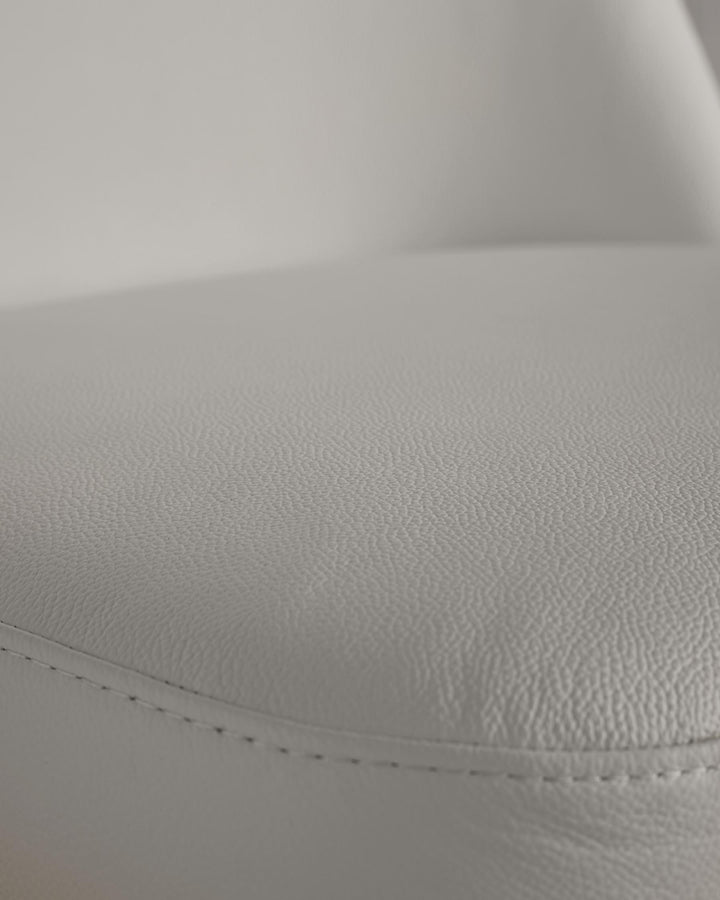 Close-up of a sleek, light grey faux leather seat, showcasing the fine texture and subtle stitching detail. Modern furniture design.