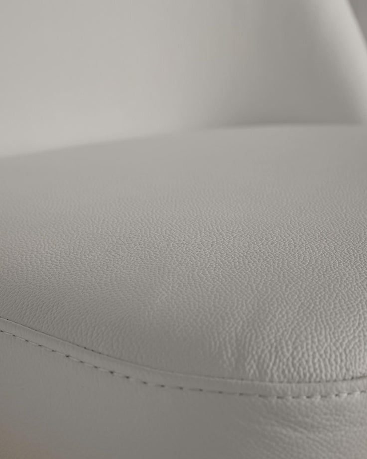 Close-up of a sleek, light grey faux leather seat, showcasing the fine texture and subtle stitching detail. Modern furniture design.