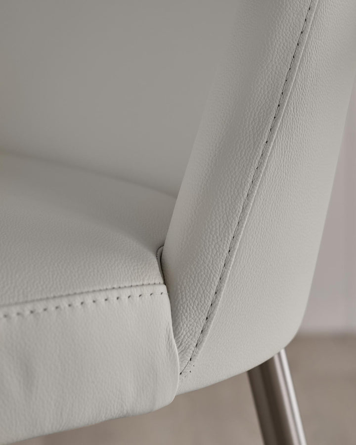 Close-up of a light grey, leather chair with stitched detailing and a brushed metal leg.