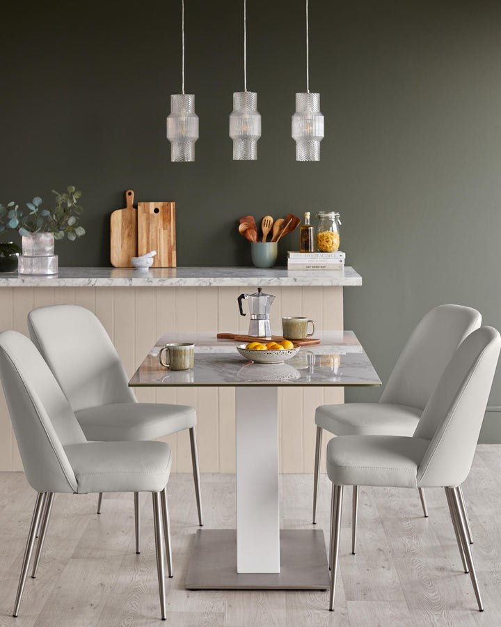A modern dining set with a marble-effect table and four grey upholstered chairs with sleek metal legs, illuminated by pendant lights.