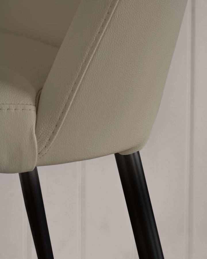 Close-up of a chair's seat and black legs, showcasing its upholstery and minimalist design, ideal for modern dining or office spaces.