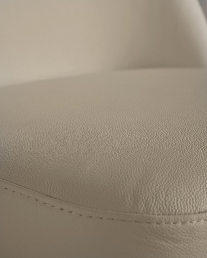 Close-up of a beige leather chair seat with stitch detailing and textured surface.