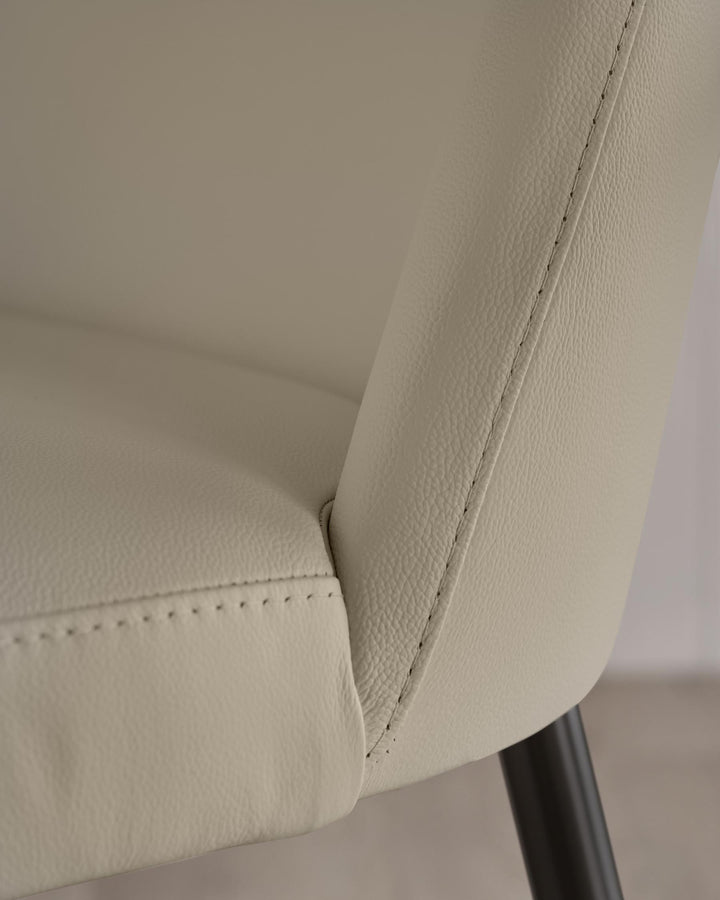 Close up of a cream-coloured leather chair with neat stitching detail and dark, round legs.