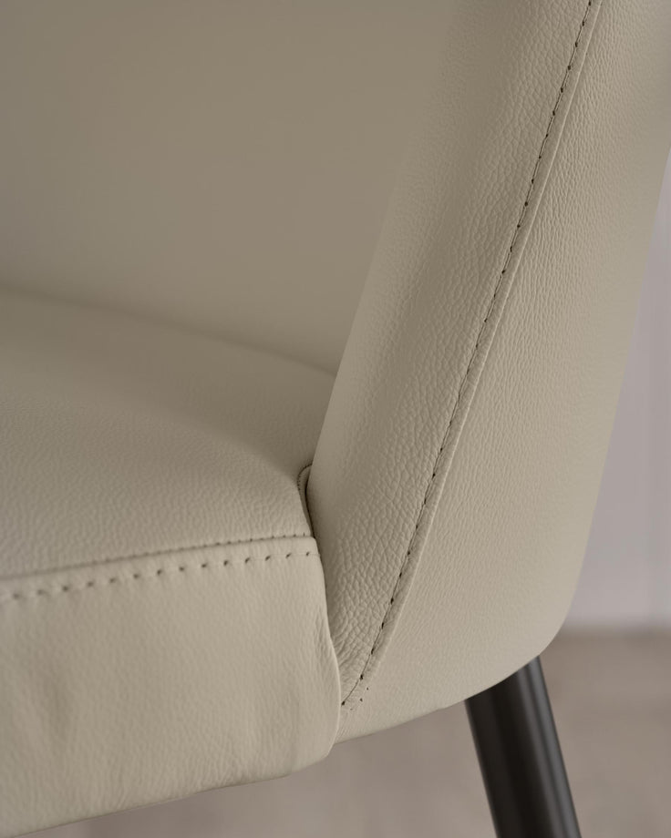 Close up of a cream-coloured leather chair with neat stitching detail and dark, round legs.