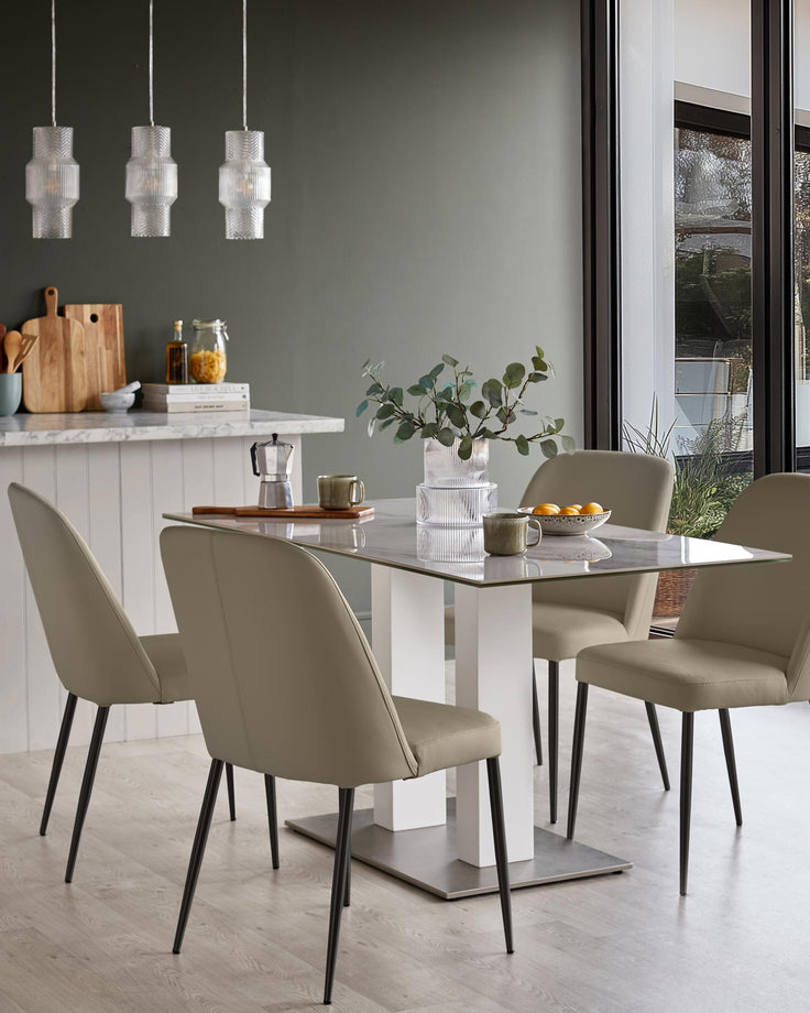A modern dining set with four chairs around a glass-topped table with a white base, lit by three pendant lights.