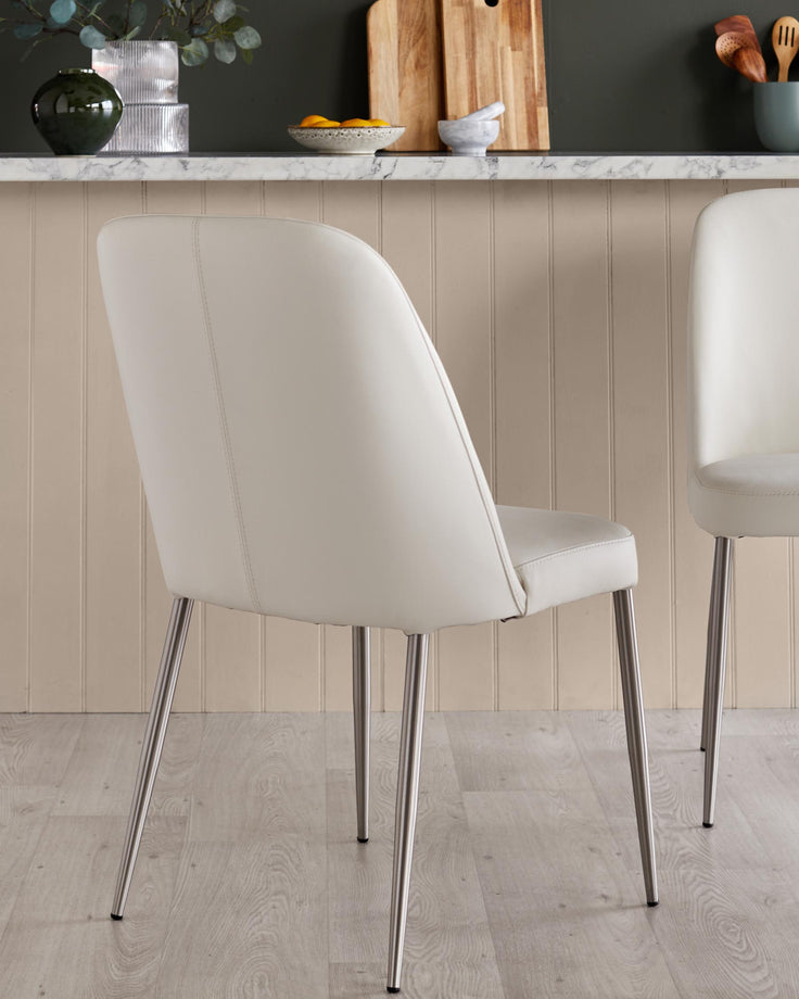 Pair of cream chairs with sleek metal legs. Stylish, contemporary design for modern dining or kitchen spaces.