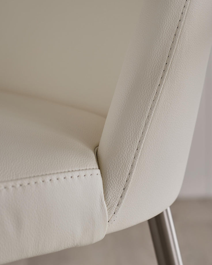 Close-up of a cream faux leather chair with neat stitching and brushed metal legs, showcasing quality craftsmanship.
