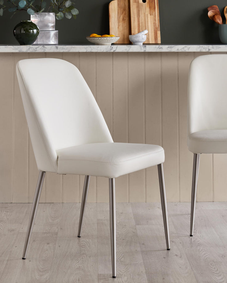 Close up of white faux leather dining chairs with sleek, silver metal legs in a kitchen setting.