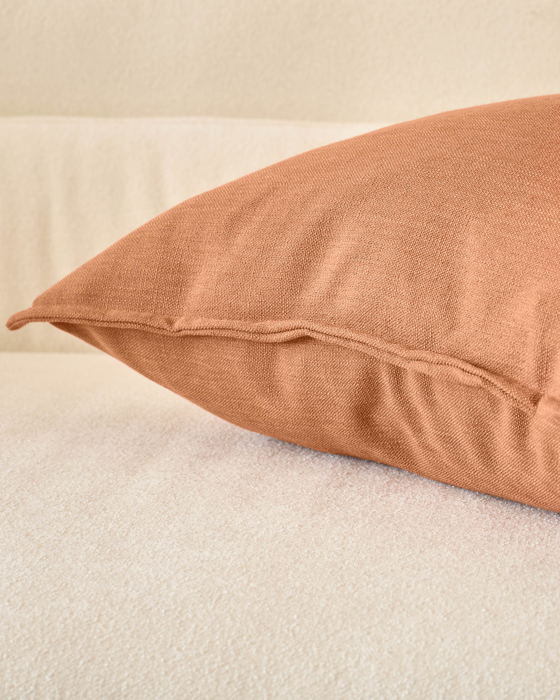 Rust-colored Delanie cushion in large size, displayed on a neutral surface showing its textured fabric and sewn seam detail.