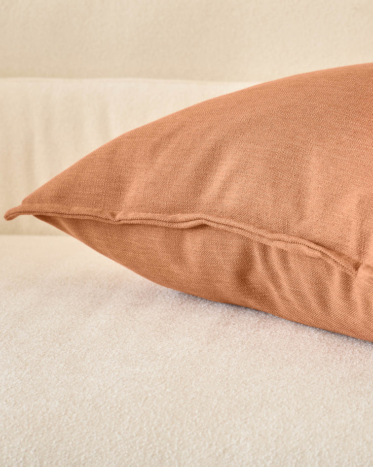 Rust-colored Delanie cushion in large size, displayed on a neutral surface showing its textured fabric and sewn seam detail.