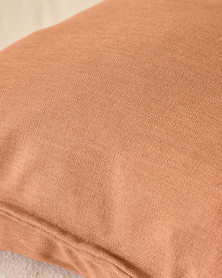 Close-up of rust-colored cushion fabric showing soft, textured weave detail.