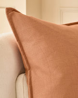 Delanie Large Rust Cushion displayed on cream upholstered furniture, showing textured weave fabric and pointed corner detail.