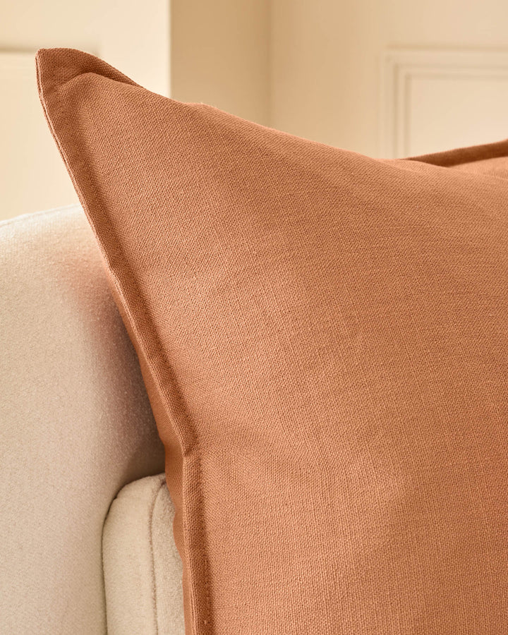 Delanie Large Rust Cushion displayed on cream upholstered furniture, showing textured weave fabric and pointed corner detail.