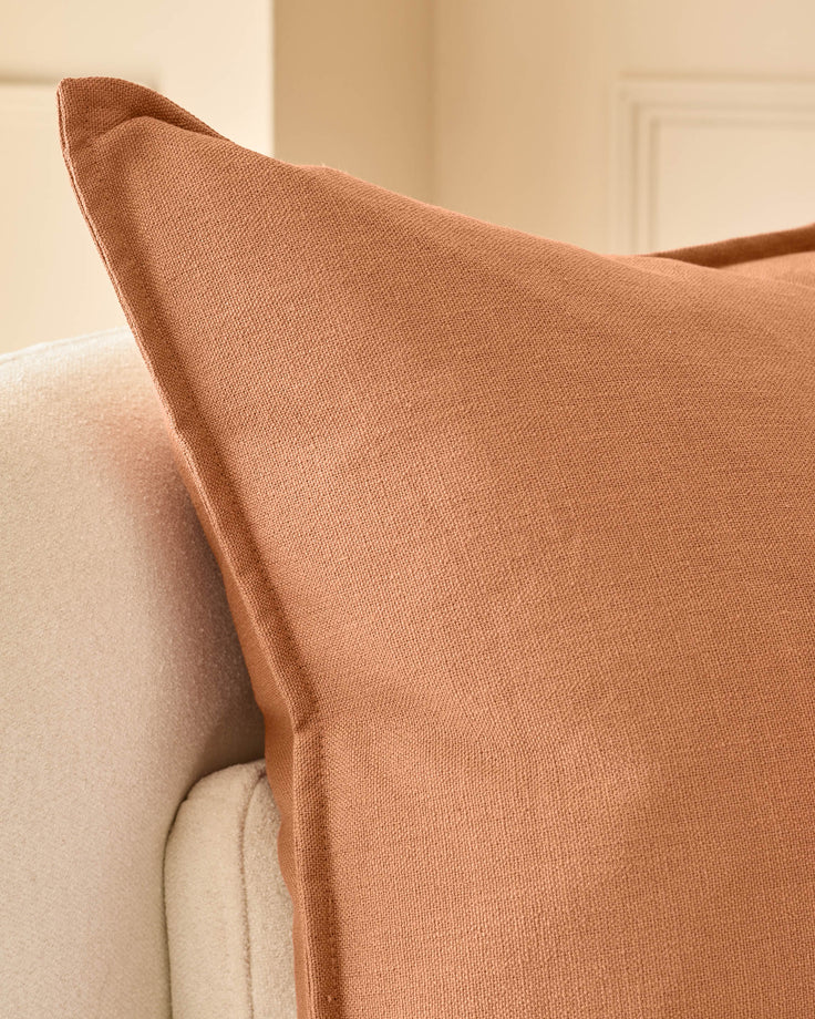 Delanie Large Rust Cushion displayed on cream upholstered furniture, showing textured weave fabric and pointed corner detail.