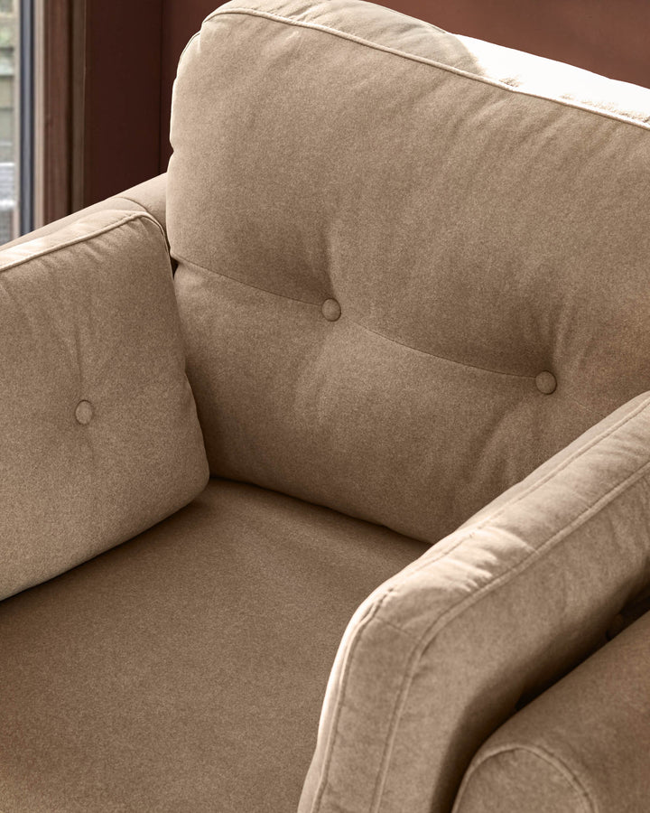 Delilah armchair in mocha fabric, showing button-tufted backrest and cushioned armrests in close-up detail.