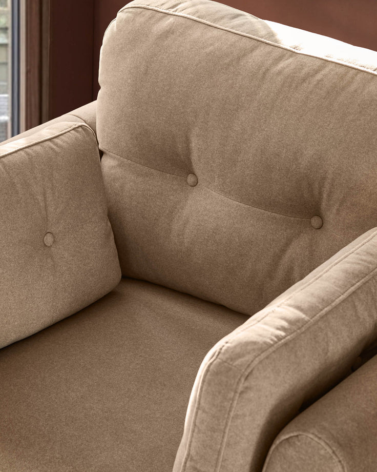 Delilah armchair in mocha fabric, showing button-tufted backrest and cushioned armrests in close-up detail.