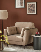 Mocha fabric armchair with rolled arms, button tufting, and tapered legs in a warm rust-colored room setting.