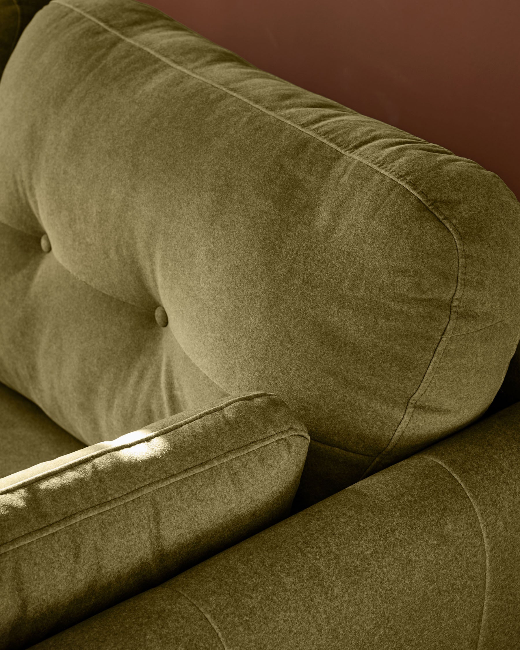Delilah 3-seater sofa in pistachio green fabric, showing tufted backrest and armrest detail from side angle.
