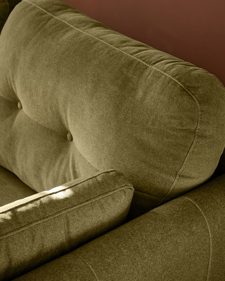 Delilah 3-seater sofa in pistachio green fabric, showing tufted backrest and armrest detail from side angle.