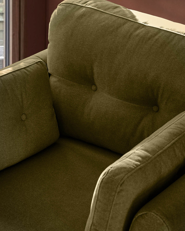 Delilah armchair in pistachio green fabric, showing tufted cushioning and curved armrests in close-up detail.